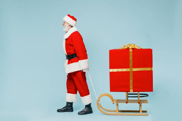 istock Full body old Santa Claus man in Christmas hat red suit clothes pull sled with big gift box go isolated on plain blue background studio. Happy New Year 2022 celebration merry ho x-mas holiday concept. 1355342476