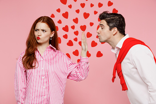 Young couple two friends woman man in casual shirt man try want kiss woman but she doing stop palm gesture and does not want it isolated on plain pink background Valentine's Day birthday party concept