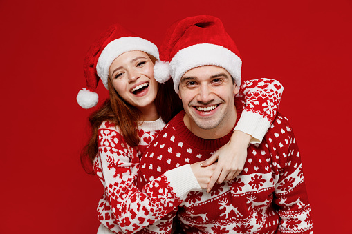 Young smiling cheerful couple friends two man woman 20s in sweater hat hugging cuddle look camera isolated on plain red background studio Happy New Year 2022 celebration merry ho x-mas holiday concept