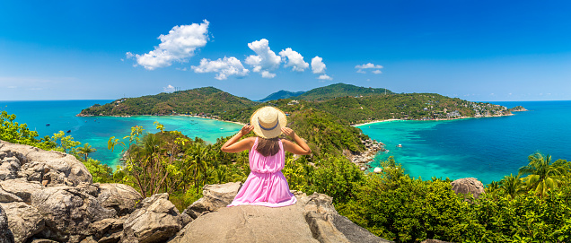 Panorama of  Woman traveler wearing pink dress and straw hat at viewpoint with Panoramic aerial view of Koh Tao island, Thailand