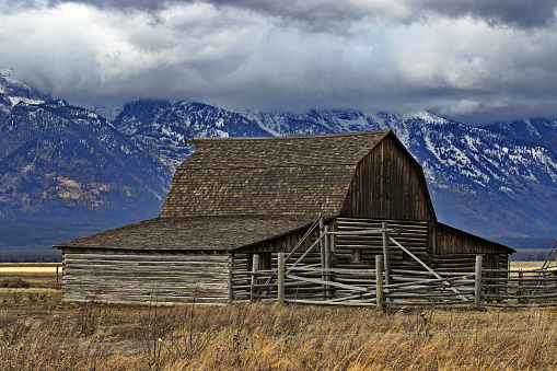 Iconic historic Moulton Barn of Mormon Row is a famous landmark in Grand Teton National Park in Wyoming reflects homesteading past. Backdrop of Teton Mountains and clouds.