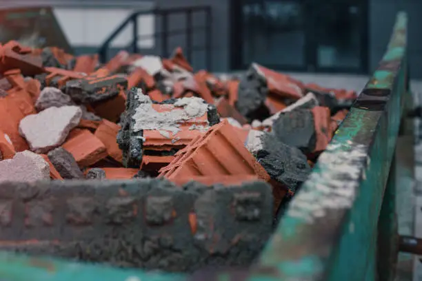 Photo of Green metal skip full of broken brick and stone material on construction site