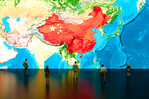 Businessman/politician figurines examine satellite view China map.