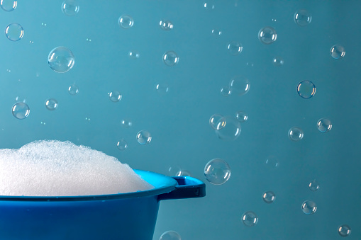 A DSLR photo of soap sud in a bowl with bubbles flying on a blue background.