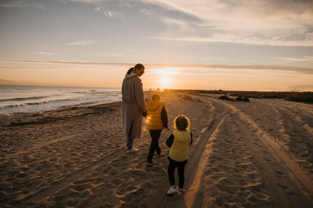 istock Mother holding hands with her children while they walking on beach 1355364082