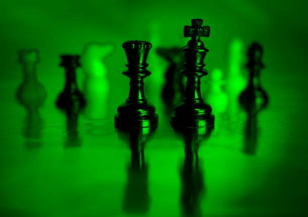 Chess pieces light painted in a moody way on a reflective surface with a water looking reflective pool. A concept image of strategy and decision making in difficult times.
