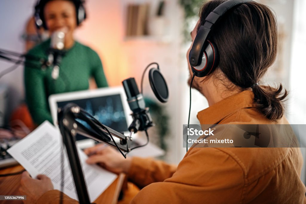 Young man and woman recording podcast Back view of young man recording podcast on interview with beautiful and successful women in studio holding paper Podcasting Stock Photo