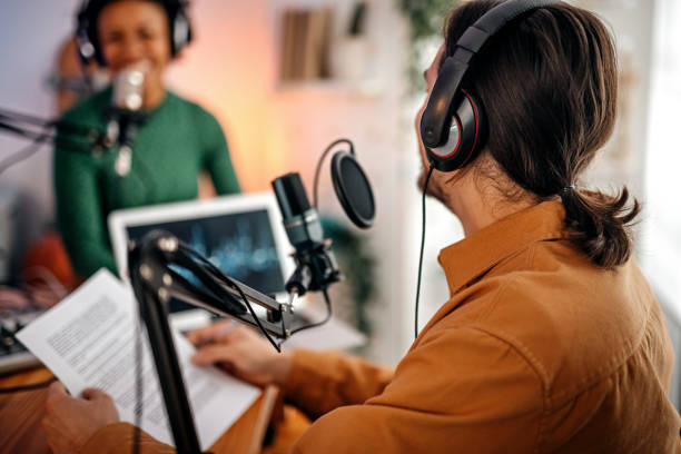 Young man and woman recording podcast Back view of young man recording podcast on interview with beautiful and successful women in studio holding paper podcasting stock pictures, royalty-free photos & images