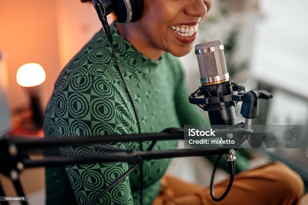 Smiling young woman recording podcast Selective focus of mouth of young smiling women recording podcast and doing live streaming using microphone and headphones in recording studio Podcasting Stock Photo