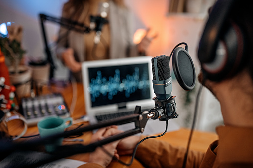 Selective focus of microphone used by young man and woman while recording podcast during interview and doing live broadcast in studio