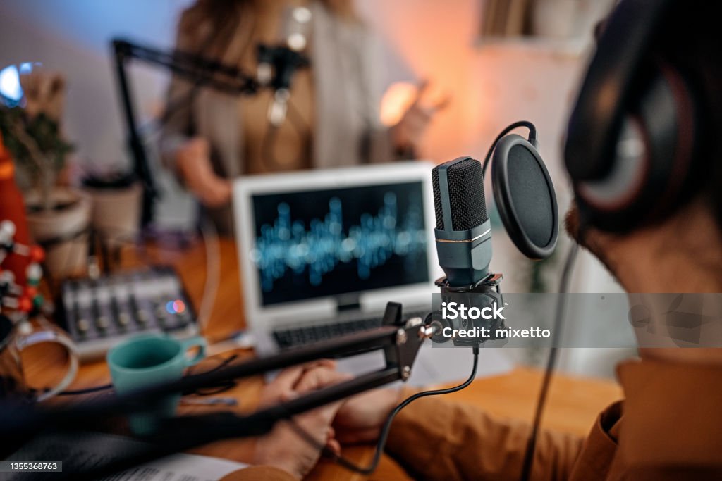 Young people recording podcast in studio Selective focus of microphone used by young man and woman while recording podcast during interview and doing live broadcast in studio Podcasting Stock Photo