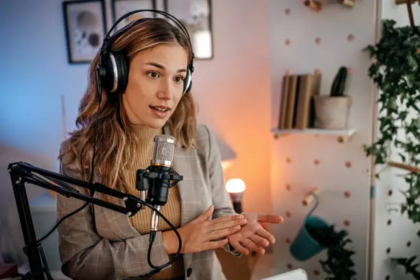 Attractive young woman blogger recording online podcast using her headphones and professional microphone in studio