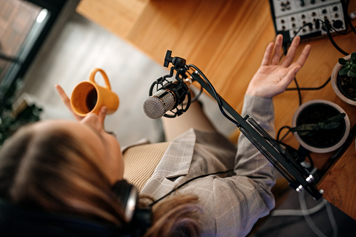 Top view of young woman recording podcast with headphones and microphone drinking coffee in recording studio