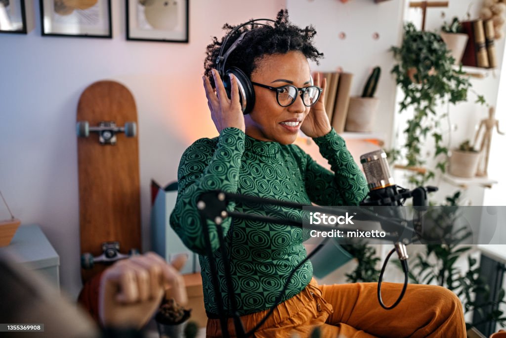 Woman setting headphones for podcast recording Young women adjusting and wearing headphones with eyeglasses while recording podcast using microphone in studio Podcasting Stock Photo