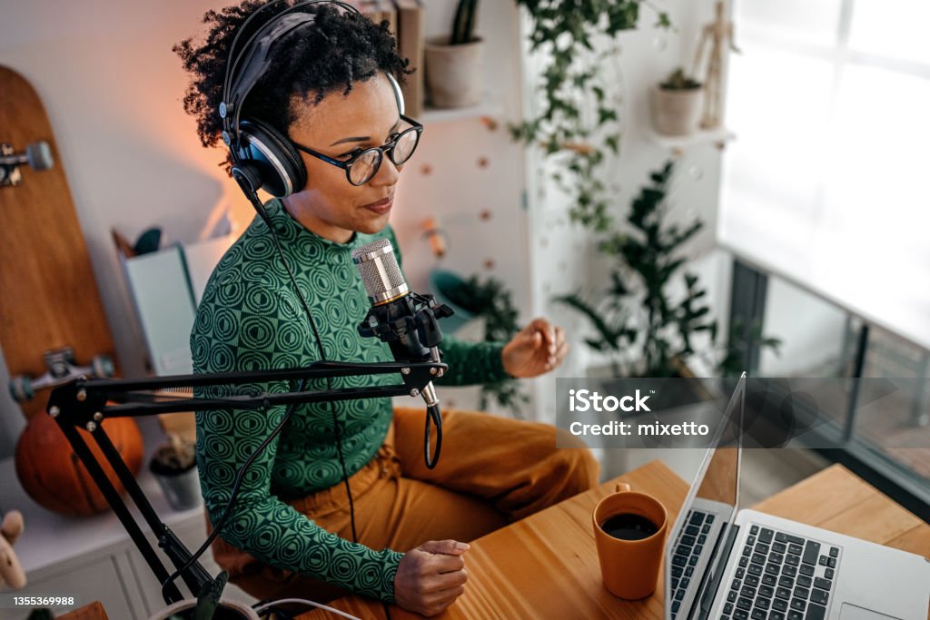 Young woman recording podcast Smiling and successful young woman recording podcast on interview in studio using equipments like microphone, laptop and headphones Podcasting Stock Photo