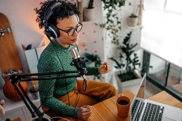 Smiling and successful young woman recording podcast on interview in studio using equipments like microphone, laptop and headphones