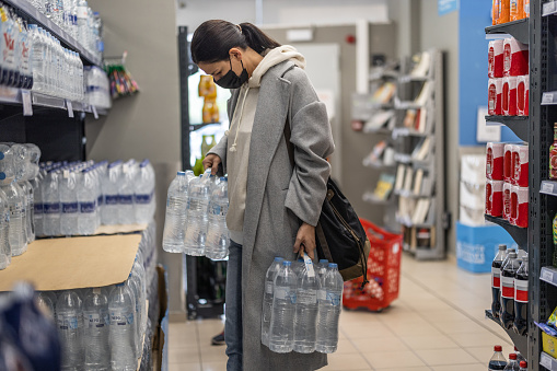 Mid age woman with face mask picking plastic water bottles from shelf