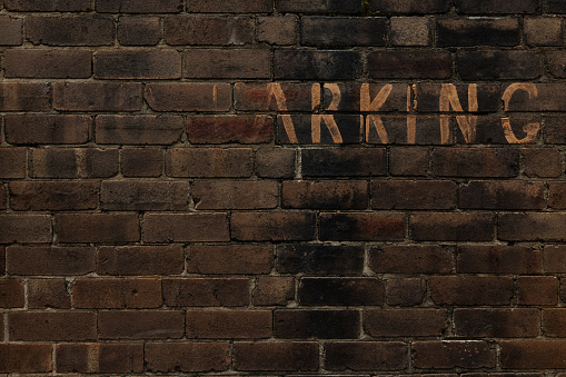 No Parking written long ago on a dirty old brick wall.