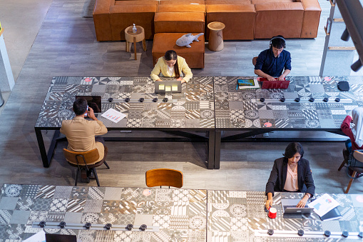 High angle view of  co-working space business office with multi racial employees working on laptop computers at workstations.