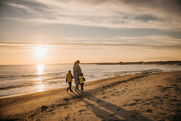 istock Mother holding hands with her children while they walking on beach 1355378505