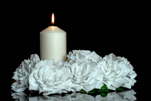 istock LIGHTED CANDLE AND WHITE ROSES ON DARK BACKGROUND. 1355380447