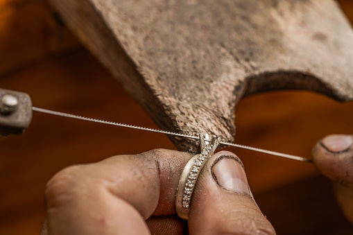 Close up view of a jeweller filing a part of a silver ring to fit a gem in a craftsman's workshop