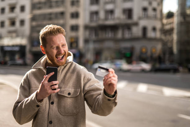 istock Happy man using online banking while on a walk on city street. 1355383308