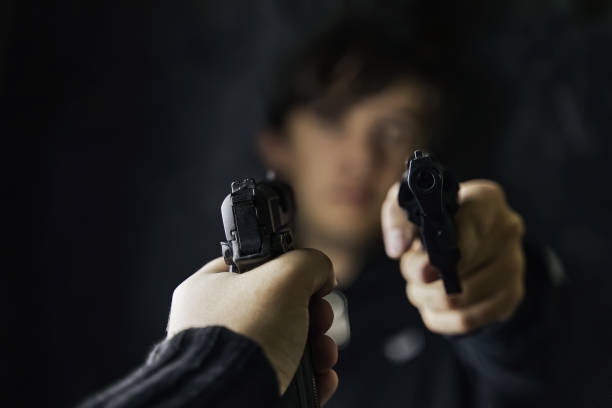 istock Man's hand with pistol pointed at criminal with revolver. 1355415645