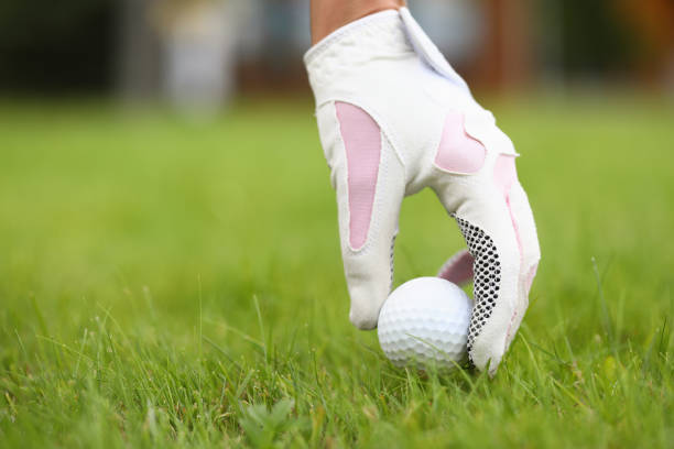A womans gloved hand puts a golf ball into position. Bright juicy grass on a golf course