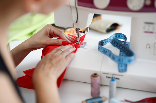 Womans hands with manicure sew on red fabric on a sewing machine. Dressmaker sews clothes in atelier