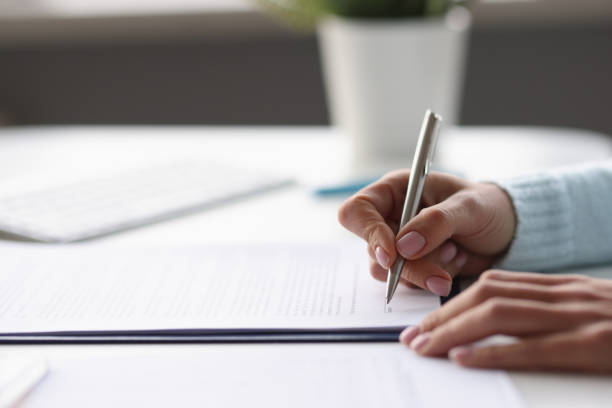 istock Woman writing with ballpoint pen in documents at table at home closeup 1355417339