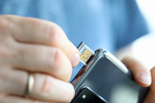 Male hands getting sim card slot of his smartphone out closeup