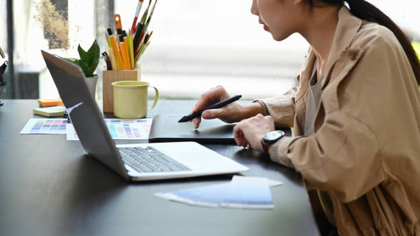 istock Cropped shot creative woman working with laptop computer and grapic tablet in office. 1355419075