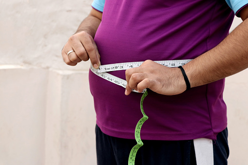 Un hombre asiático mide su vientre gordo con una cinta métrica sobre un fondo liso photo