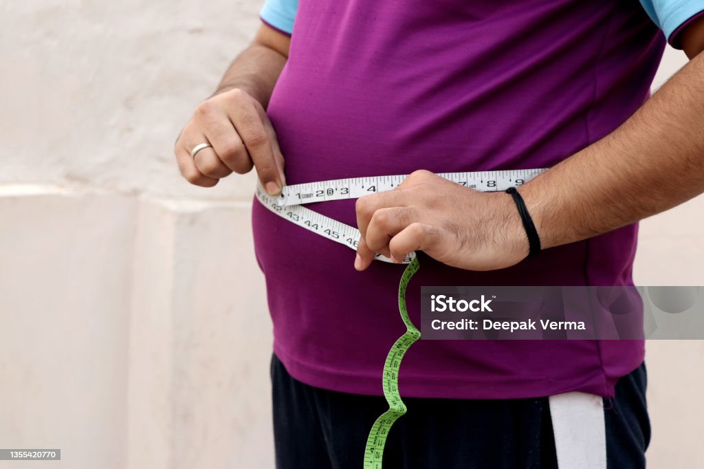 A asian men measures his fat belly with a measuring tape on a plain background Obesity Stock Photo