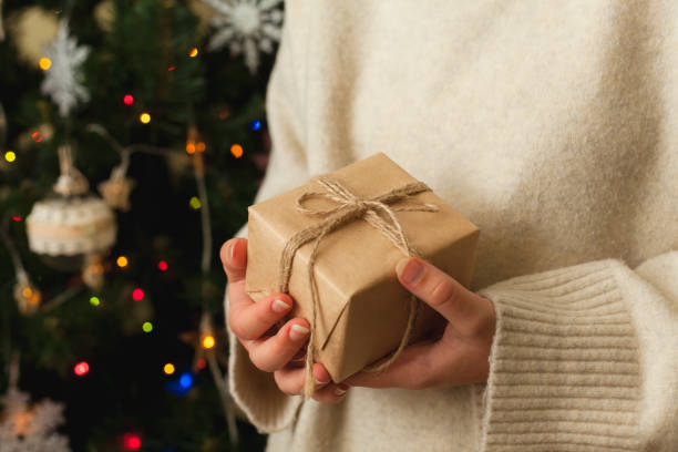 istock girl holding small gift in her hands. decorated Christmas tree on background. 1355426268