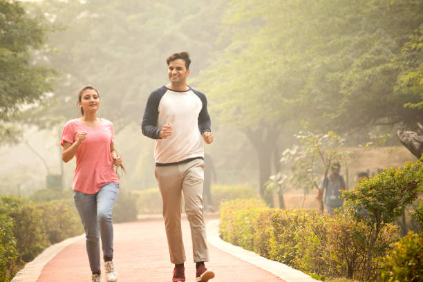 Healthy couple jogging in nature Happy couple talking while jogging on footpath at park indian man walking in park stock pictures, royalty-free photos & images