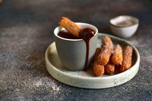 Traditional spanish dessert churros - fried choux pastry with chocolate sauce Traditional spanish dessert churros - fried choux pastry with chocolate sauce on a plate on a dark slate, stone or concrete background. choux pastry photos stock pictures, royalty-free photos & images