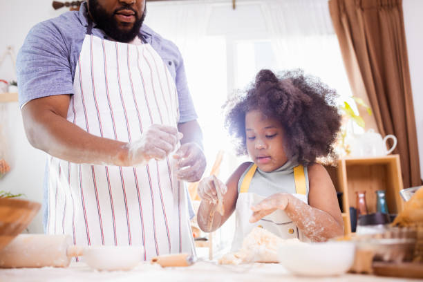 istock Happy African American father and daughter having fun while preparing cookie dough at home. happy family time. 1355439935