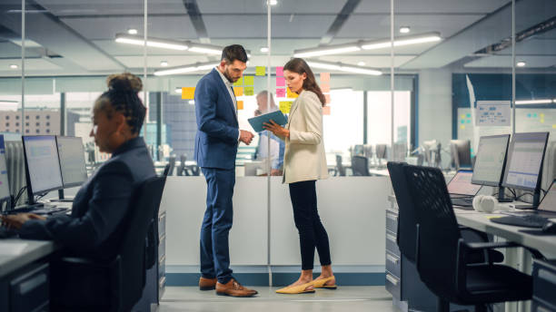 istock Young Manager Creating Project Plan with Experienced Colleague on Office Wall with Paper Notes. Employees Discuss Business, Financial and Marketing Projects. Specialists Work in Diverse Team. 1355440507
