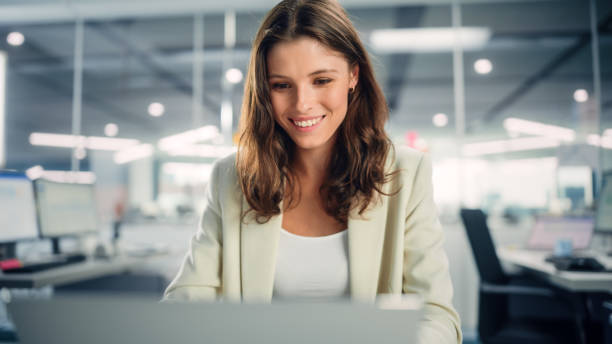 istock Young Happy Businesswoman Using Computer in Modern Office with Colleagues. Stylish Beautiful Manager Smiling, Working on Commercial, Financial and Marketing Projects. Specialist in Diverse Team. 1355440563