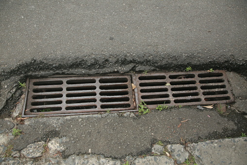 Iron grill drains on the edge of the asphalt road.