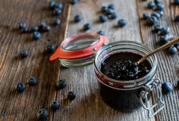 Fresh and homemade blueberry jam served in a jar with spoon isolated on wooden table