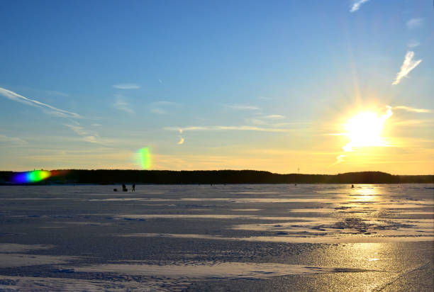 Fishermen on a frozen lake catch fish in a hole of ice on the background of evening sunset. Fishermen on a frozen lake catch fish in a hole of ice on the background of evening sunset. Winter arrives, bodies of water freeze over, making them prime spots for ice fishing. man ice fishing stock pictures, royalty-free photos & images