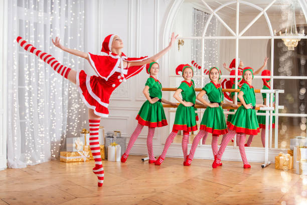 istock Children dressed as elves and practicing at a ballet barn look at a dancing ballerina dressed as santa claus in a spacious white studio. 1355446580