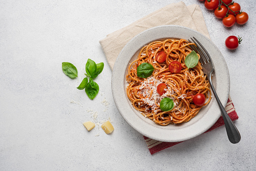 Spaghetti pasta with tomato sauce, basil and cheese in plate on light background, top view
