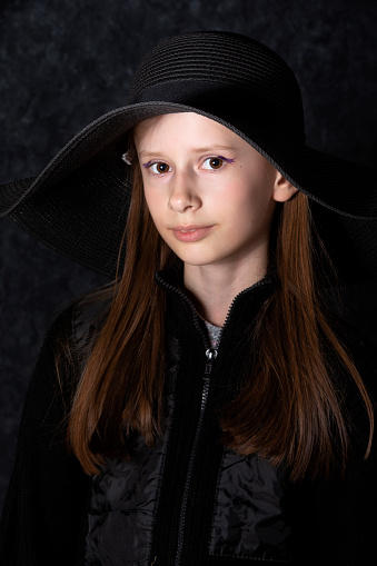 Portrait of a little girl in a black hat on a dark background.