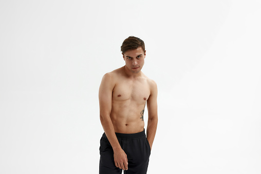 Young confident caucasian ballet dancer with hand in pocket looking at camera. Handsome guy with naked torso and tattoo. Person wearing ballet pants. Isolated on white background in studio. Copy space