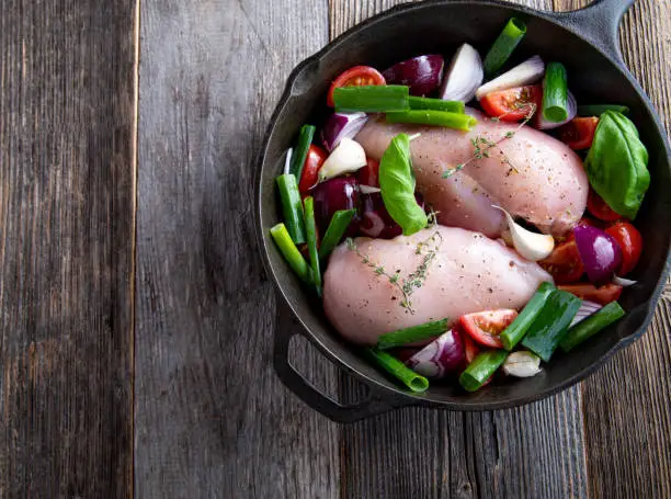 Healthy cooking with a low fat chicken breast and vegetables. Served raw and uncooked in a rustic pan isolated on wooden table. Overhead view with copy space