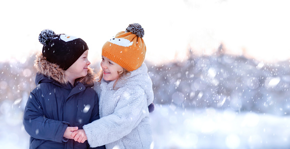 A little boy and a girl hugging and smiling under the snow in the forest